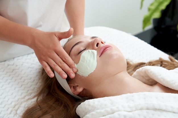 Premium Photo Cosmetologist Applying Rejuvenating Facial Mask On A Female Face In Beauty Salon
