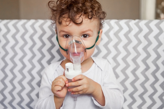 Cough treatment by inhalation. baby with a nebulizer in his hands, breathing mask on his face Premium Photo