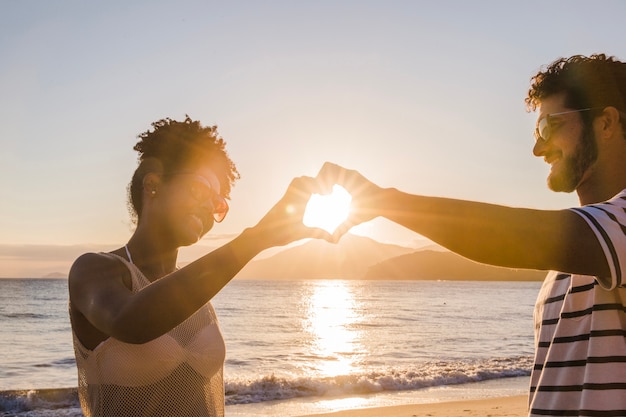 free-photo-couple-forming-heart-with-hands-at-sunset