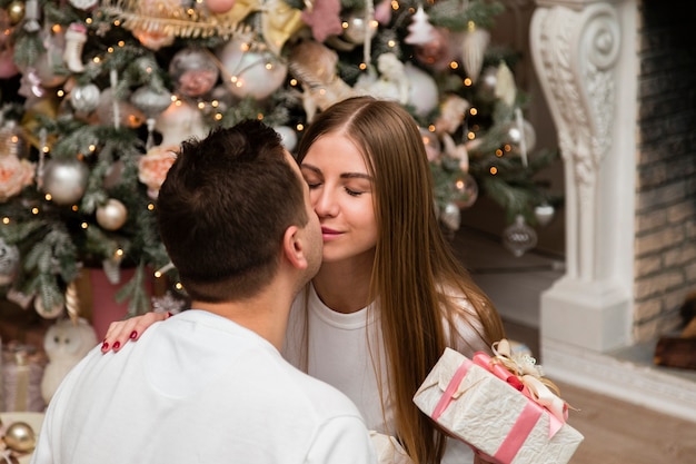 カップルがクリスマスツリーの前でギフトとキス 無料の写真