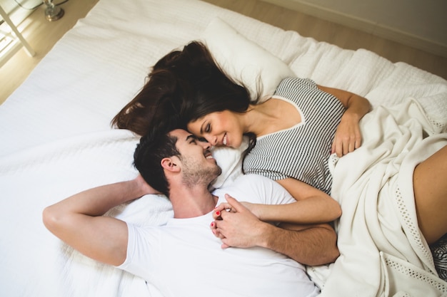 Couple lying on the bed holding hands and looking into each other's eyes Free Photo