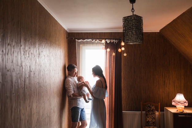 Couple Standing Near The Window Playing With Their Baby At Home Free