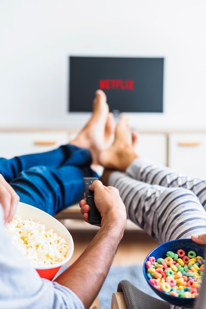 Couple with snacks using remote control while watching series Free Photo