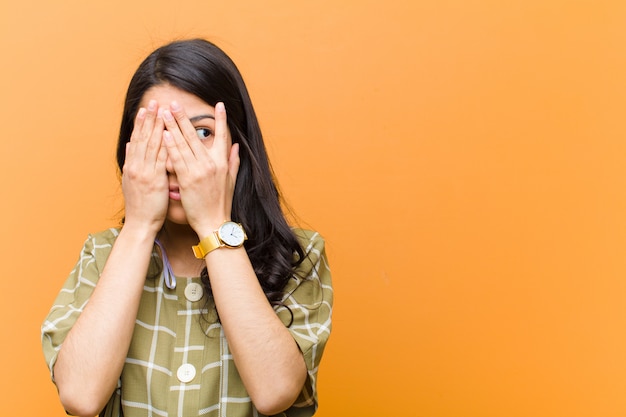 Premium Photo | Covering face with hands, peeking between fingers with ...