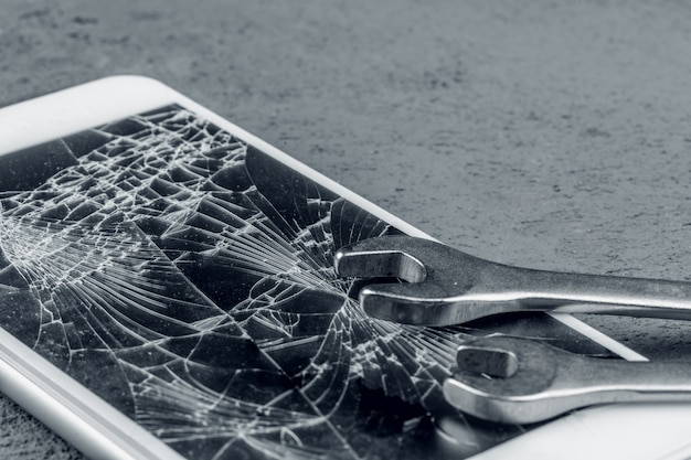 Crashed smartphone with repairing tools on grey wall Premium Photo