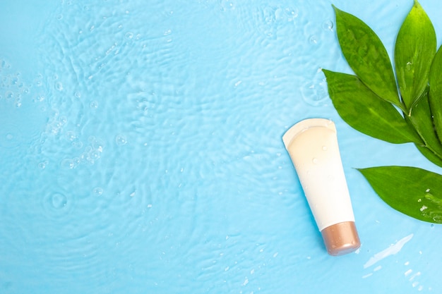 Cream lotion to skin with green leaves on blue water surface of pool, top view. Premium Photo