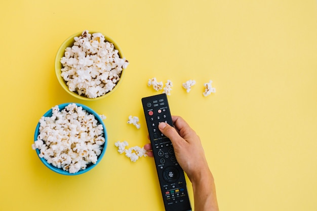 Crop hand with remote control near popcorn Free Photo