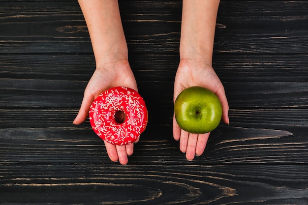 Crop hands holding donut and apple Free Photo