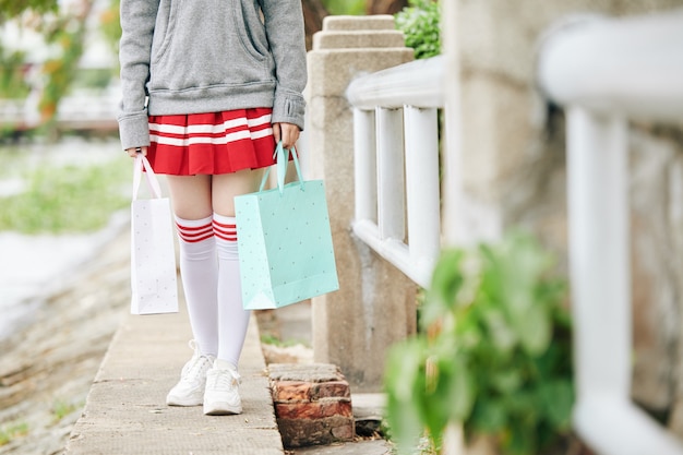 屋外を歩くときに紙袋を保持している短いスカートと太もものハイソックスの女子高生のトリミングされた画像 プレミアム写真