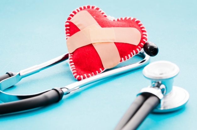 Crossed bandage over the red soft fabric heart and stethoscope on blue background Free Photo