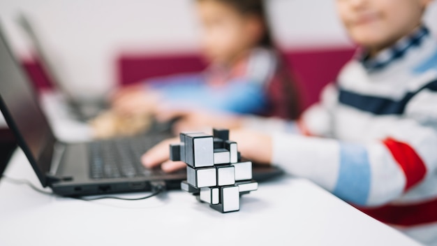 Cube puzzle in front of girl using laptop on white desk