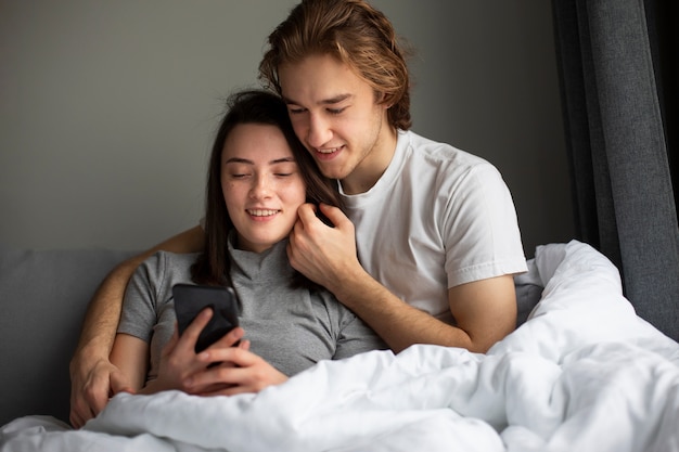 ベッドでスマートフォンを見て抱きしめるカップル 無料の写真