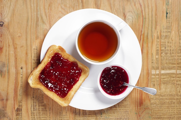 Premium Photo | Cup of tea and toast with jam on old wooden table. top view