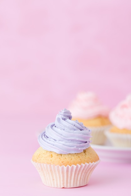 カップケーキはパステル調のピンクの背景にピンクと紫のバタークリームで飾られています プレミアム写真
