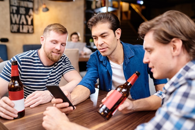 Premium Photo | Curious men reading news on phone while drinking beer ...