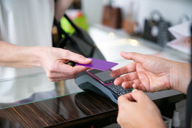 Customer giving credit card to cashier over desk with pos terminal for payment. cropped shot, closeup of hands. shopping concept Free Photo