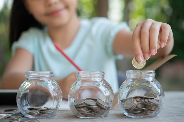 cute asian little girl playing with coins making stacks of money,kid saving money into piggy bank, into glass jar. child counting his saved coins, children learning about for the future concept. free photo