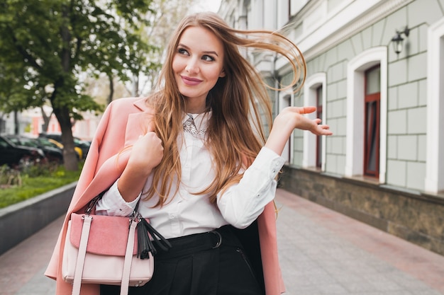 Cute attractive stylish smiling woman walking city street in pink coat spring fashion trend holding purse, elegant style Free Photo