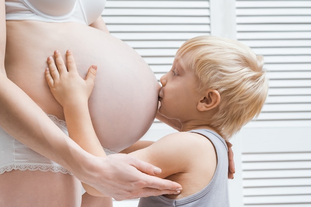 妊娠中のお母さんのおなかにキスして抱き締めるかわいい男の子 2番目の妊娠の概念 プレミアム写真