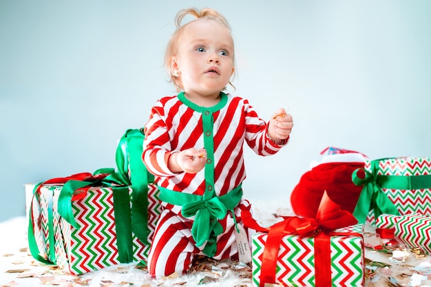 クリスマスの背景にポーズをとってサンタ帽子に近い1歳のかわいい赤ちゃん女の子 クリスマスボールが付いている床に座っています 連休シーズン 無料の写真