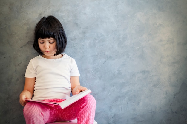 Cute Black Hair Little Girl Reading Book By The Wall Photo