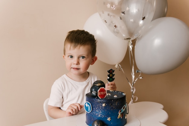 3歳のかわいい男の子が彼の誕生日を祝って おいしい美しいケーキを食べています 風船を持った子供の写真 プレミアム写真
