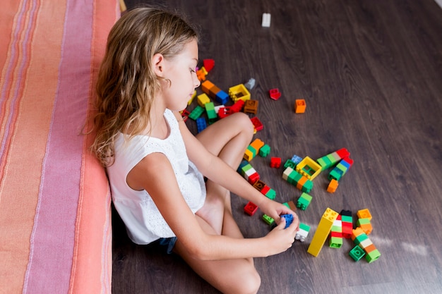 自宅でタワーを構築建設おもちゃブロックで遊ぶかわいい面白いプレティーンの女の子 遊ぶ子供たち デイケアの子供たち 子供とおもちゃ 家族のライフスタイル プレミアム写真