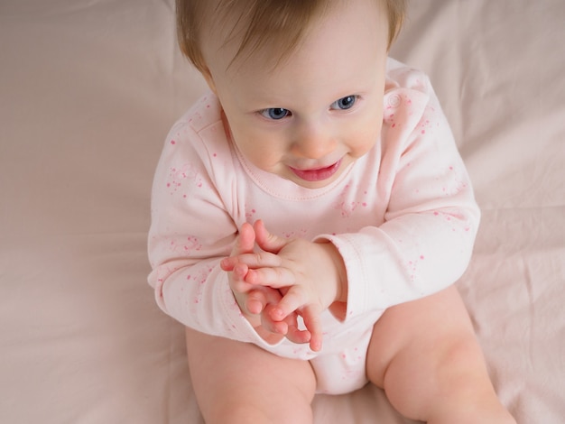 かわいい優しい女の赤ちゃん 生後10ヶ月 ベッドに座って 手をたたく 笑顔 クローズアップ ピンクの色調の女の子の肖像画 ベビー用品のコンセプト プレミアム写真