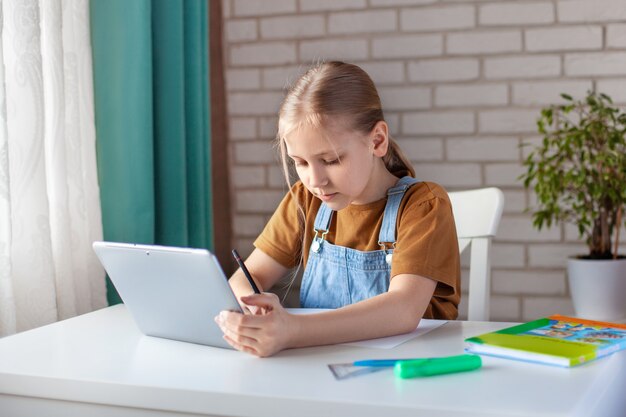 Premium Photo A Cute Girl Does Her Homework Using A Tablet