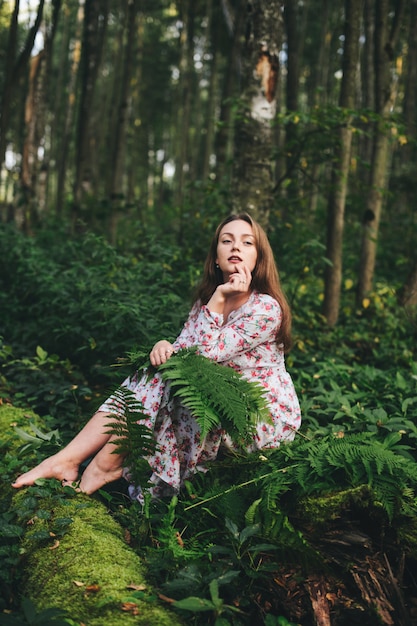 Premium Photo A Cute Girl In A Floral Dress Is Sitting With A Fern Bouquet In The Forest