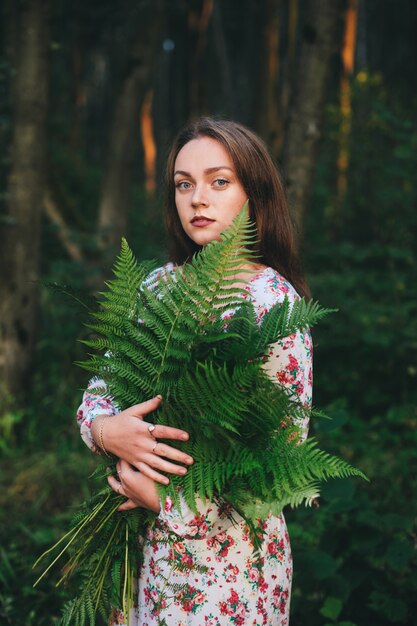 Premium Photo A Cute Girl In A Floral Dress Is Sitting With A Fern Bouquet In The Forest