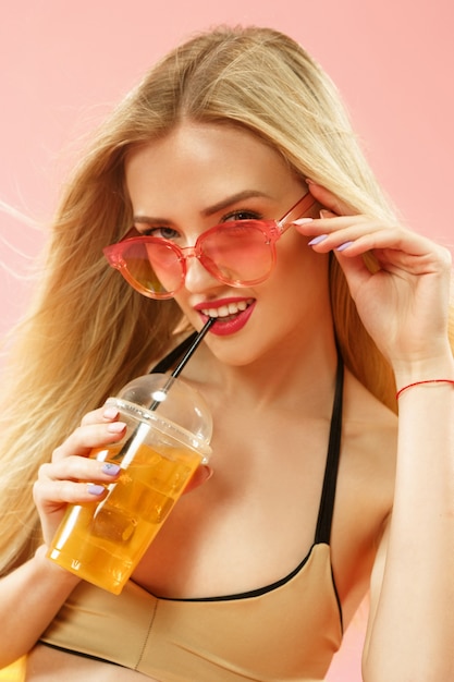 スタジオでポーズをとってオレンジジュースを飲む水着のかわいい女の子 ピンクの夏の肖像画白人ティーンエイジャー 無料の写真