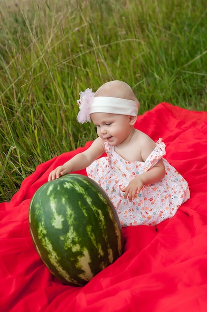 スイカと草の中で8ヶ月の青い目の女の子とかわいい幸せなブロンド 健康的な食事 子供時代 果物の熟度 子育て 季節の収穫の概念 自然の夏の完璧な白人の 赤ちゃん プレミアム写真