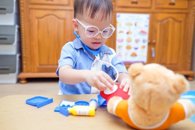 かわいいアジア2歳幼児男の子子供自宅でぬいぐるみで医者を遊んで 子供が聴診器を持ってテディベアグッズを調べる プレミアム写真