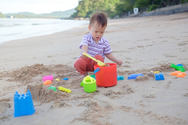 かわいい小さなアジア2歳の幼児男の子座って 美しい砂浜の熱帯のビーチで子供のビーチおもちゃを遊んで プレミアム写真