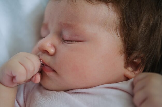 白い格子縞の上に眠っている黒髪のかわいい女の赤ちゃん 育児と出産の概念 口の中で 新生活 幸せな家族 家に 愛 甘い 優しさ プレミアム写真