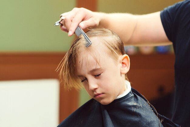 理髪店で美容師に散髪されているかわいい男の子 子供に髪型をしている床屋の男 はさみで美容師 理髪店 子供時代 少年のための新しい髪型 プレミアム写真