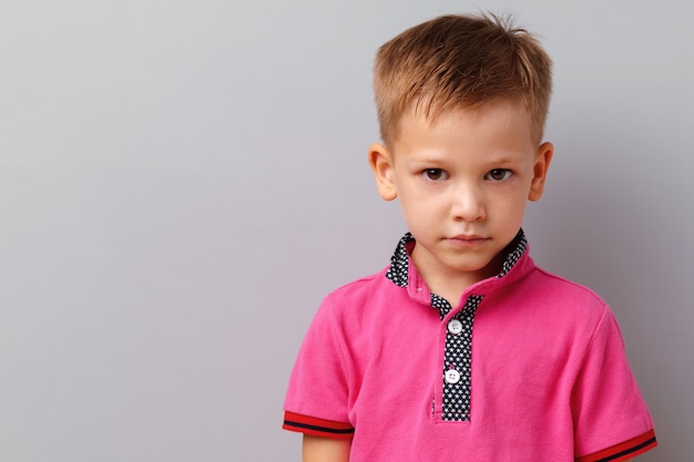 灰色の背景に対してポーズピンクのtシャツでかわいい男の子 プレミアム写真