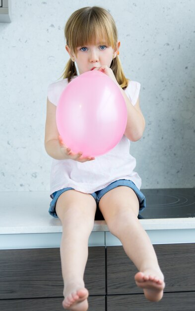 キッチンにピンクの風船を膨らますかわいい女の子 無料の写真