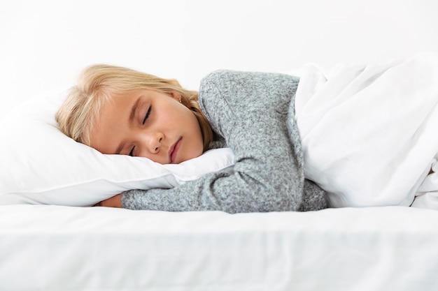 楽しい夢を持っている灰色のパジャマの白い枕で寝ているかわいい女の子 無料の写真