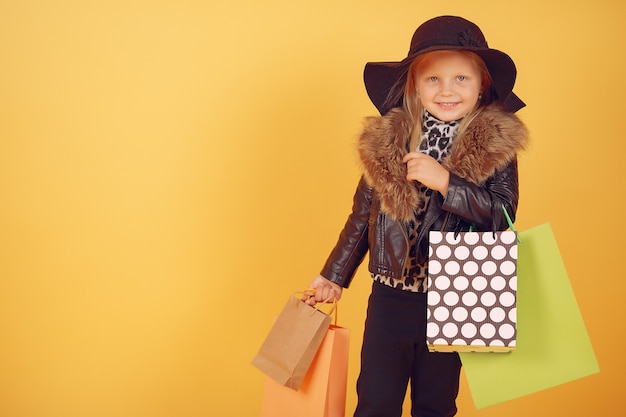 Cute little girl with shopping bags on a yellow background Free Photo
