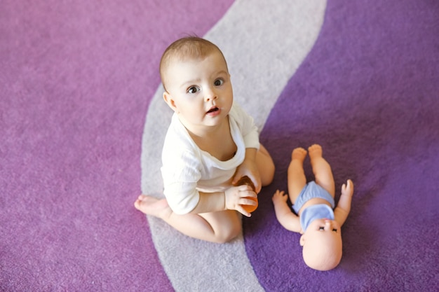 人形と紫のカーペットの上に座ってかわいい素敵な赤ちゃん女性 無料の写真