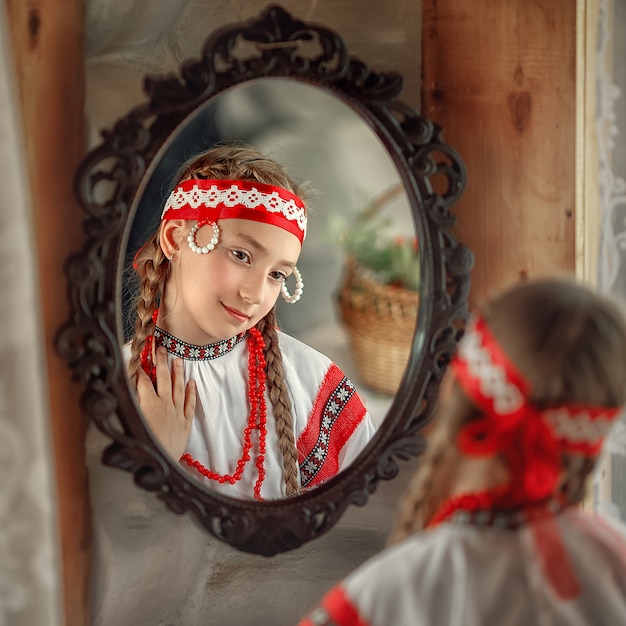 民族衣装のかわいいロシアの女の子が鏡を見る プレミアム写真