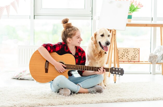 屋内で素敵な犬とギターを弾くかわいい10代の少女 プレミアム写真