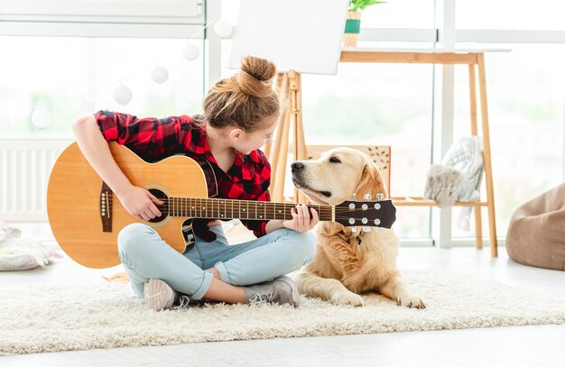 屋内で素敵な犬とギターを弾くかわいい10代の少女 プレミアム写真