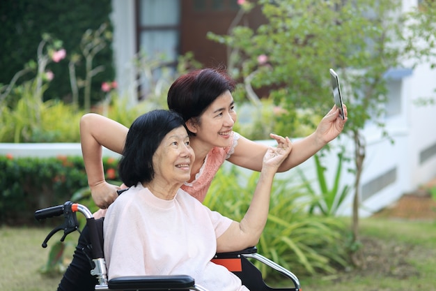 Daughter caring for the elderly asian woman ,do selfie, happy, smiles in backyard. Premium Photo