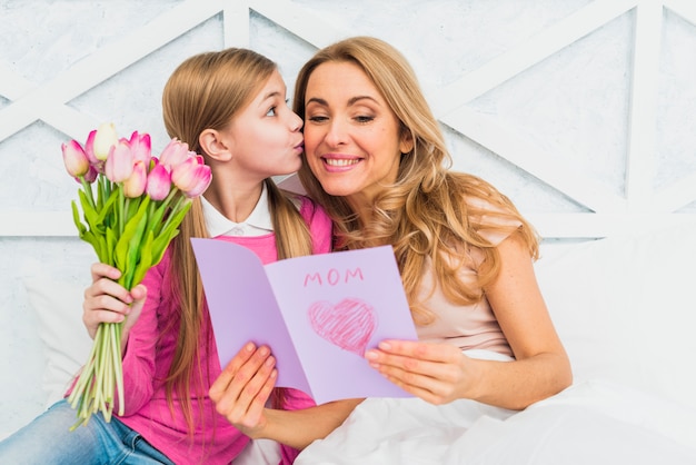 Daughter kissing mother with greeting card Free Photo