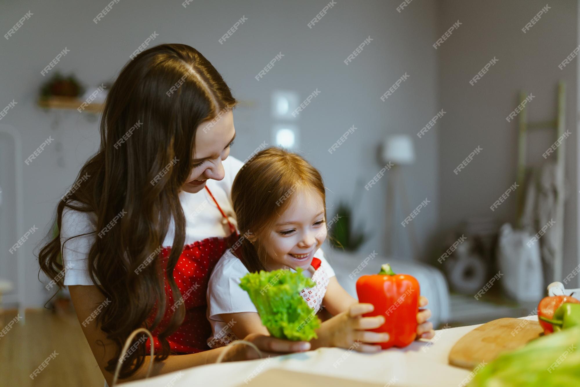 Premium Photo Daughter Sits In Her Mothers Arms And They Sort Vegetables Together In The Kitchen 2557