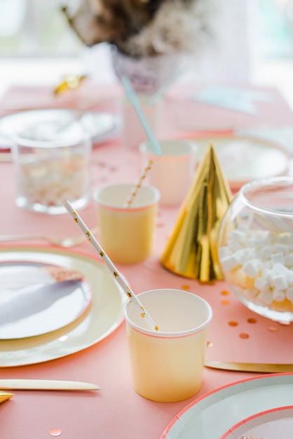 テキスタイルピンクのテーブルクロス 紙のカラフルなカップ プレートとカクテルストローで子供のパーティーディナーの装飾的なお祝いテーブルの設定 お誕生日おめでとうデコレーション プレミアム写真
