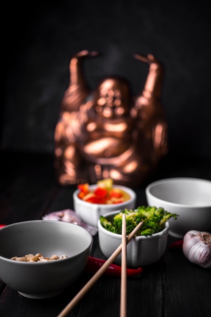 Defocused statue with cups of vegetables and chopsticks Free Photo